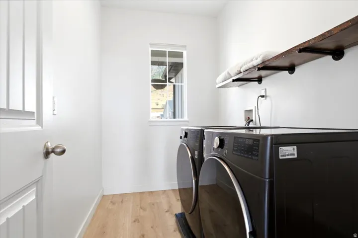 Dedicated laundry space featuring wood-finish flooring, a window providing natural light, and a built-in wood shelf with black iron brackets