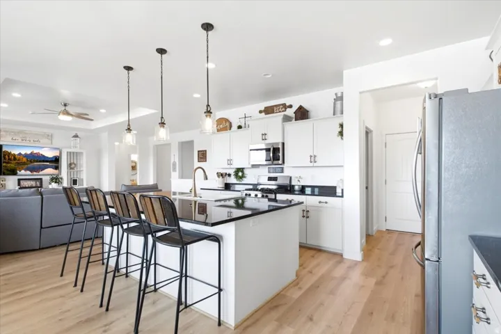 Open-concept kitchen featuring white cabinetry, black countertops, stainless steel appliances, and wood-finish flooring