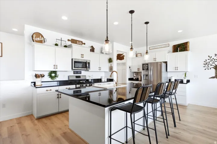 Open-concept kitchen featuring an expansive center island with seating, pendant lighting, stainless steel appliances, white cabinetry, and wood-finish flooring