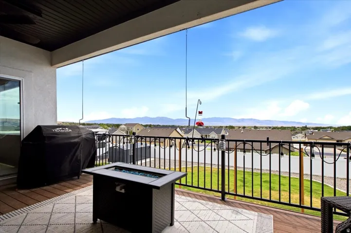 Covered outdoor deck with wood-finish flooring, featuring a black metal railing and mountain scenery
