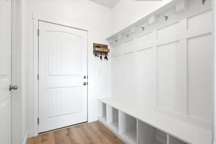 Mudroom entry featuring light wood-finish flooring, a white paneled door, and a built-in storage bench with cubbies