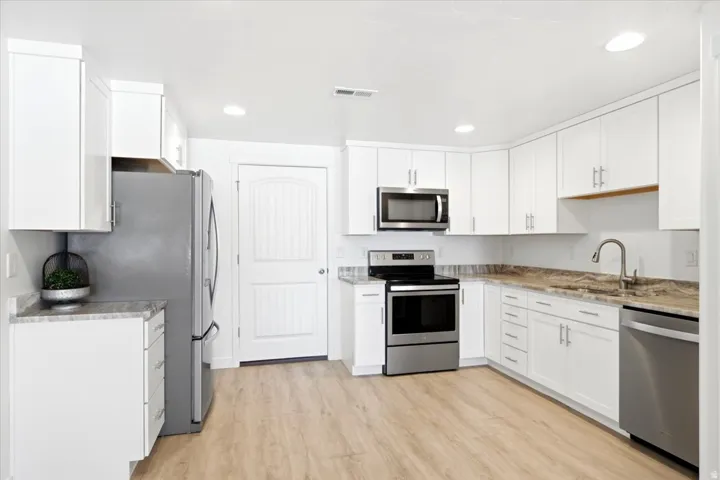 Kitchen featuring white cabinetry, wood-finish flooring, stainless steel appliances, recessed lighting, and stone countertops