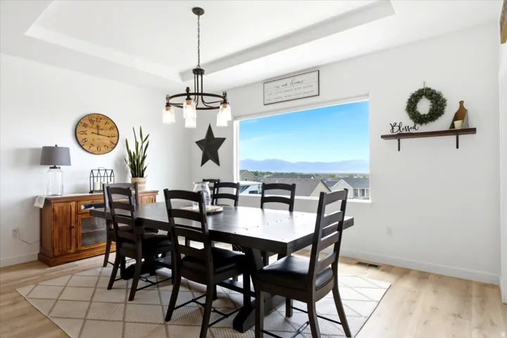 Spacious dining area featuring a large picture window, tray ceiling, and a modern chandelier