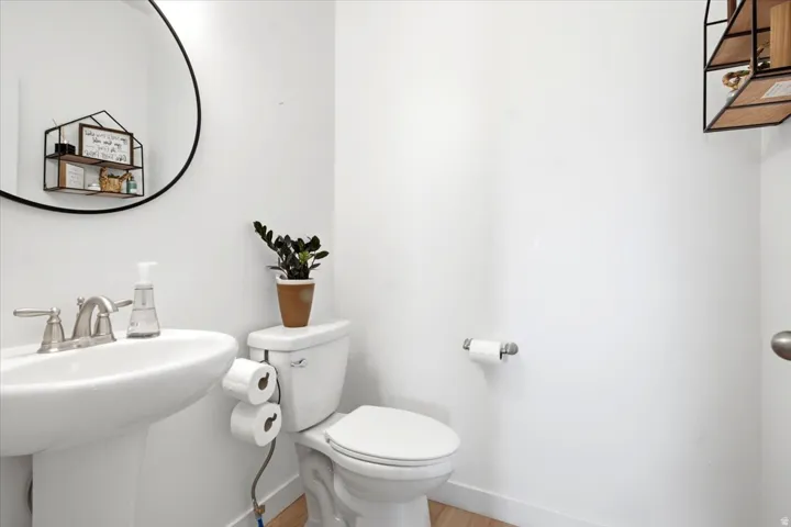Pedestal sink with brushed nickel faucet, round wall mirror, and light wood-finish flooring