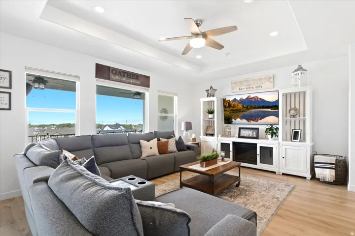 Living space featuring wood-finish flooring, a tray ceiling with recessed lighting and a ceiling fan, and large windows