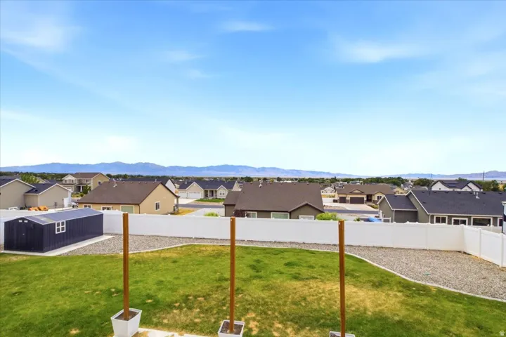 Expansive backyard featuring a green lawn, gravel landscaping, a dark blue storage shed with white trim, and a white privacy fence