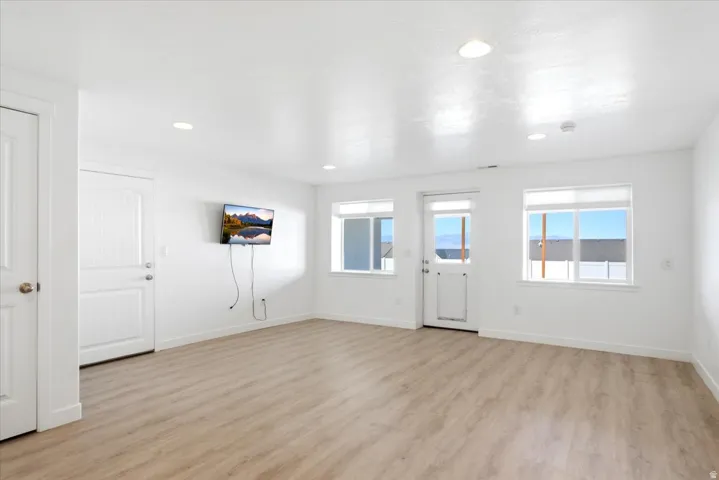 Recessed ceiling lighting, wood-finish flooring, multiple windows, and a glass-paneled exterior door