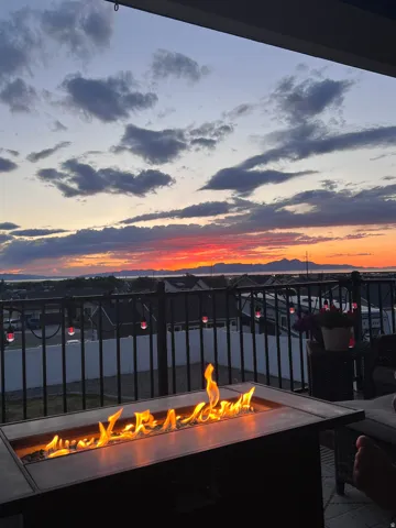 Outdoor patio featuring a rectangular fire pit, metal railing, and string lighting