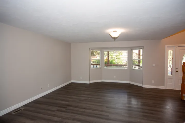 Spacious room featuring dark wood-finish flooring, light neutral-toned walls, and white baseboards