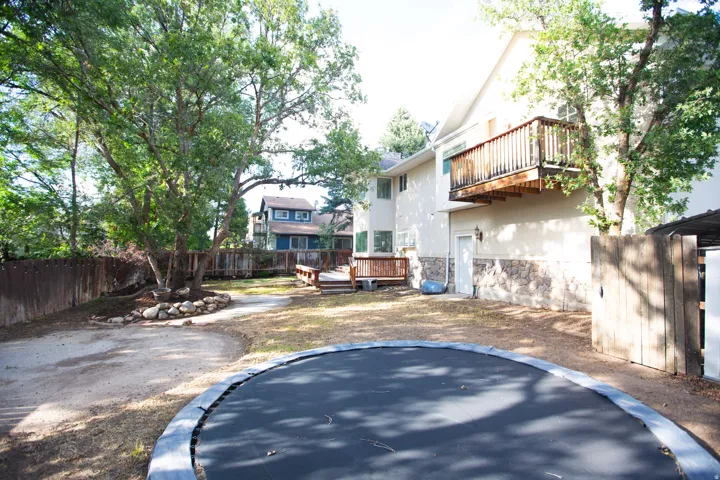 Expansive yard featuring mature trees, a multi-level wood deck, a stone facade on the lower level, and a second-story wood balcony, with in ground tramp