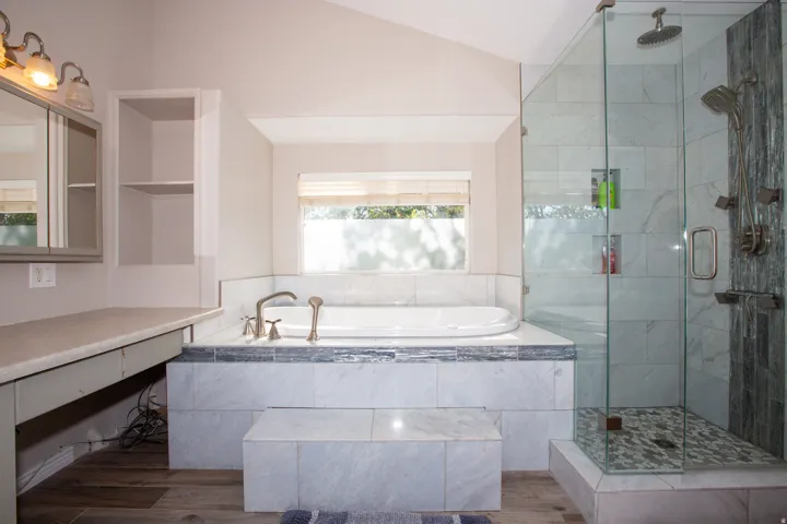 Master bath with soaking tub with bronze-finish fixtures, a glass-enclosed shower with multiple sprayers, tile flooring, and built-in vanity with mirror