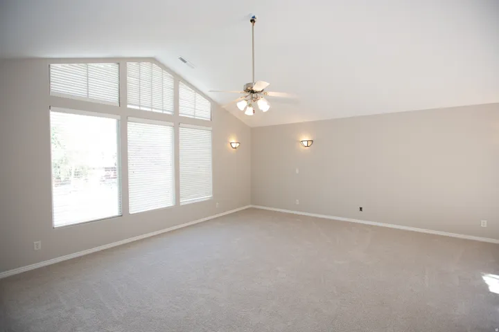 Master suite with vaulted ceiling featuring a large window array with blinds, ceiling fan, and sconce lighting