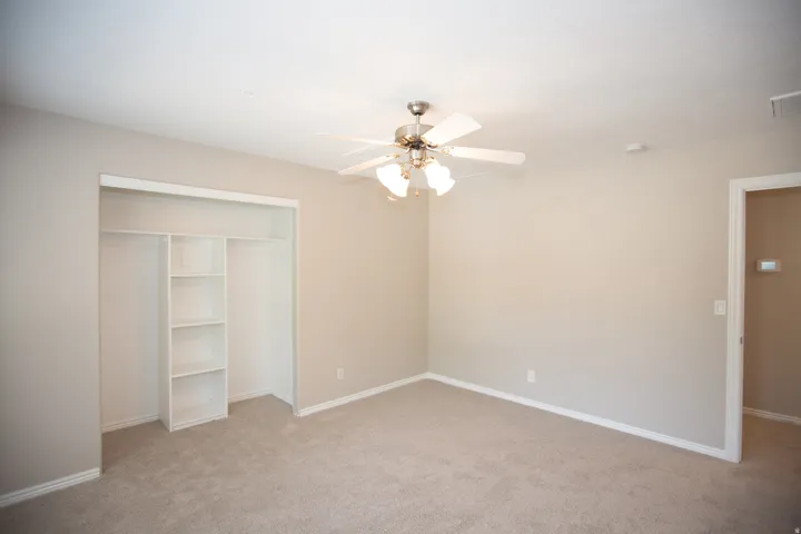 Neutral-toned bedroom featuring wall-to-wall carpeting, a ceiling fan with integrated lighting, and a closet with built-in shelving