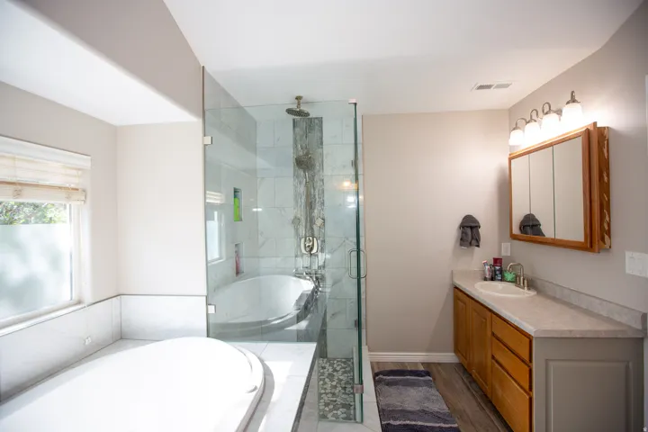 Master bath featuring a glass-enclosed shower with a rain showerhead, a separate soaking tub, and a vanity with a surface-mounted sink and wood cabinetry