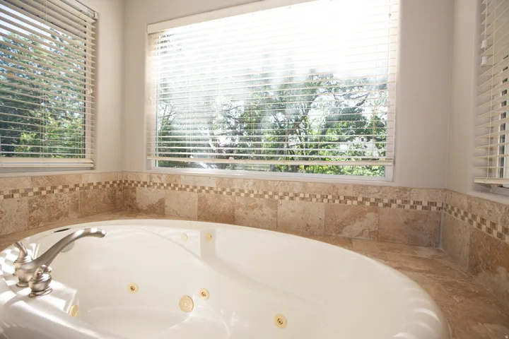 Built-in jetted tub with deck-mounted faucet, surrounded by natural stone tile with an accent mosaic border