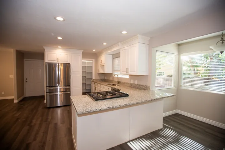 Contemporary kitchen featuring white cabinetry, granite countertops, a stainless steel refrigerator, and a built-in gas range on the island