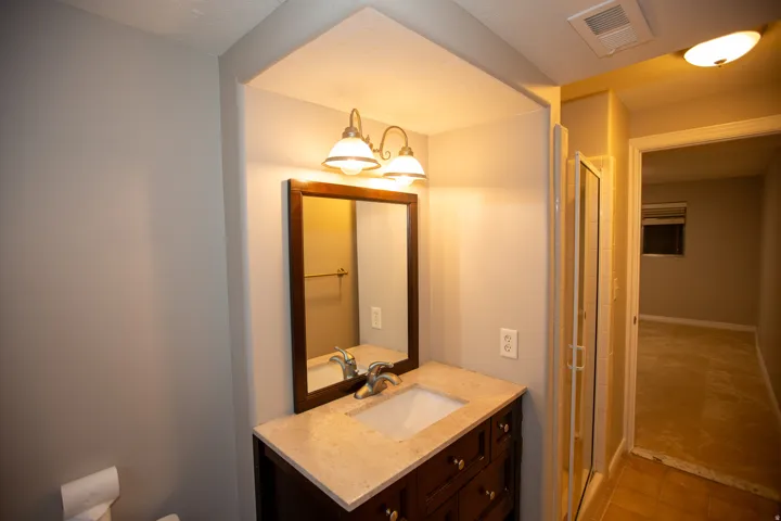 Bathroom vanity featuring a light-toned countertop, under-mount sink, shower and dark wood-finish cabinetry