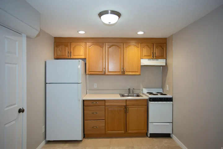 Compact kitchen featuring light wood cabinetry, white appliances, and a tiled floor