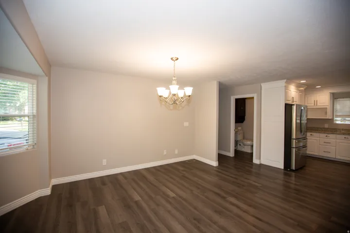 Open-concept living space featuring wood-finish flooring, a contemporary chandelier, neutral wall tones, white trim, and a kitchen with white cabinetry and stainless steel appliances