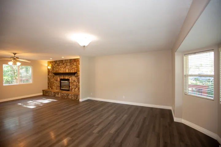 Spacious room featuring wood-finish flooring, a stone-clad fireplace with hearth, recessed lighting, and ample natural light from multiple windows