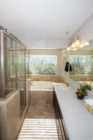 Bathroom featuring a glass-enclosed shower, a built-in jetted tub, and a vanity with an integrated sink