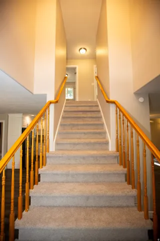 Two-story entryway with a carpeted staircase, light-toned wall paint, and natural wood handrails and balusters
