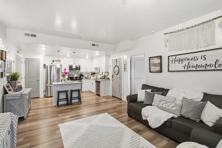 Open-concept living space featuring wood-finish flooring, a contemporary kitchen with white cabinetry, stainless steel appliances, a kitchen island with seating, and recessed lighting