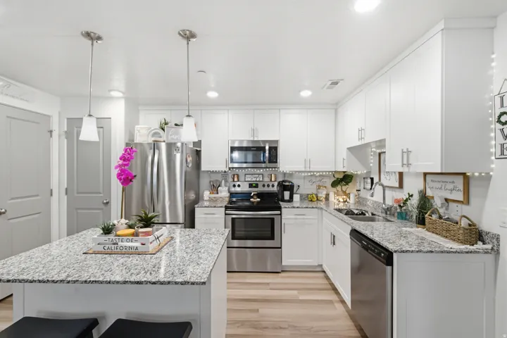 Modern kitchen featuring a central island with granite countertop, white cabinetry, stainless steel appliances, and wood-finish flooring