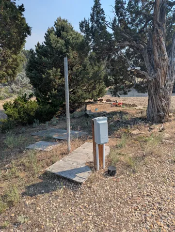 Utility hookups on a gravel surface, surrounded by natural landscaping and mature trees