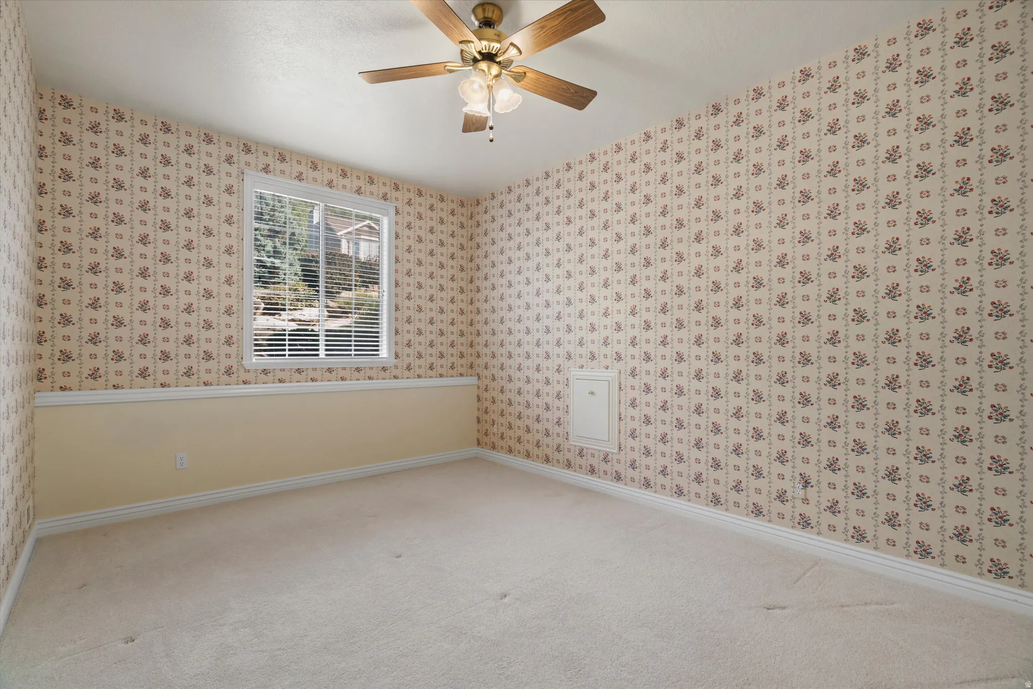 Carpeted interior space featuring patterned wallpaper, a single window with horizontal blinds, a ceiling fan with integrated lighting, and a white access panel