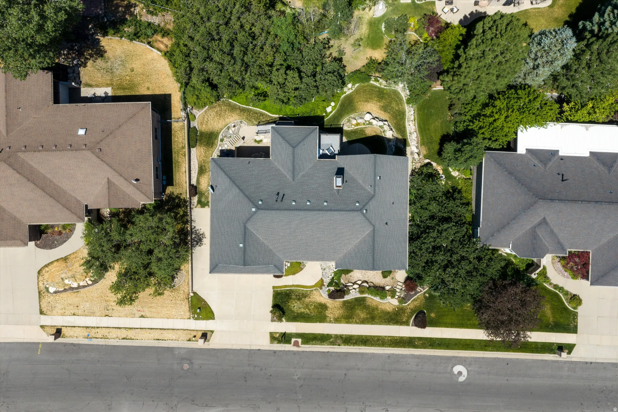 Gable roofline property featuring a driveway, mature landscaping, paved patio, and stone accents