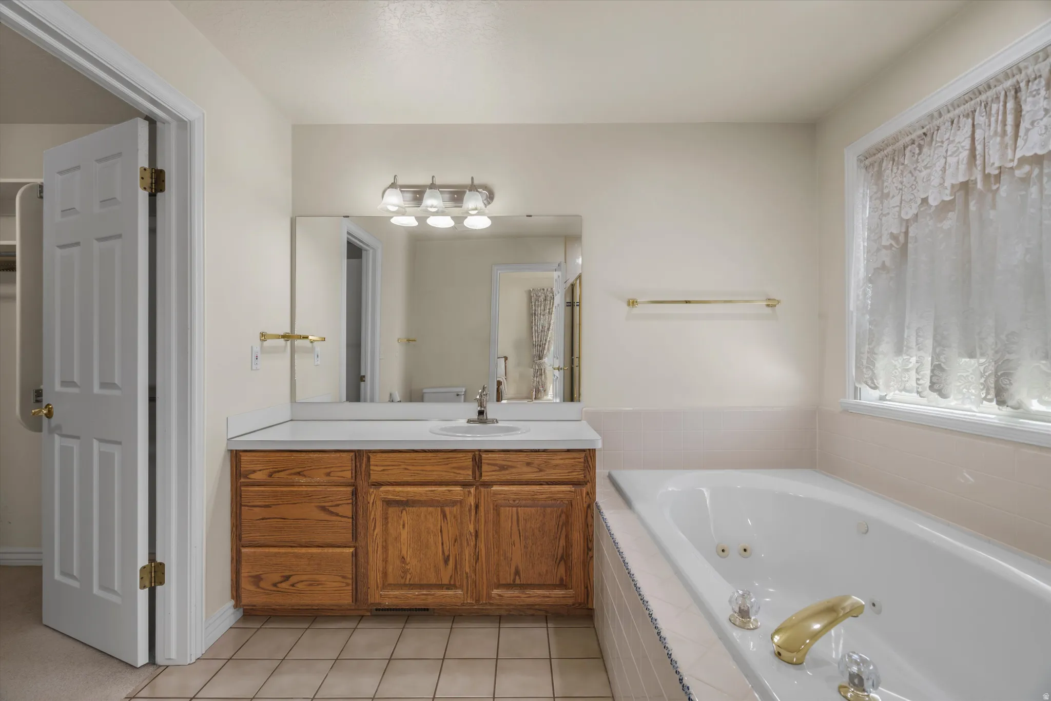 Bathroom featuring a built-in jetted tub, wood-finish vanity with countertop, wall-mounted mirror, and tile flooring