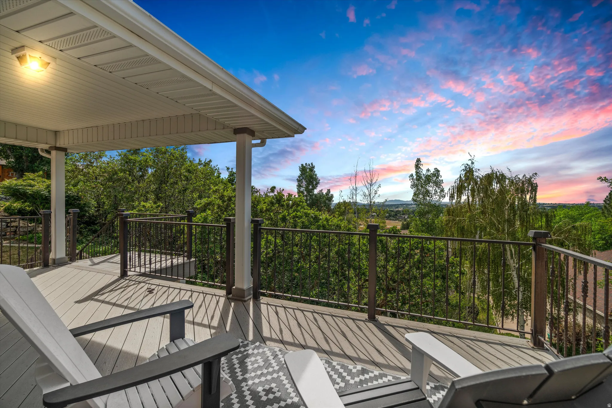 Spacious covered deck featuring composite decking, white soffit, dark brown railing with black balusters, and expansive tree-lined scenery