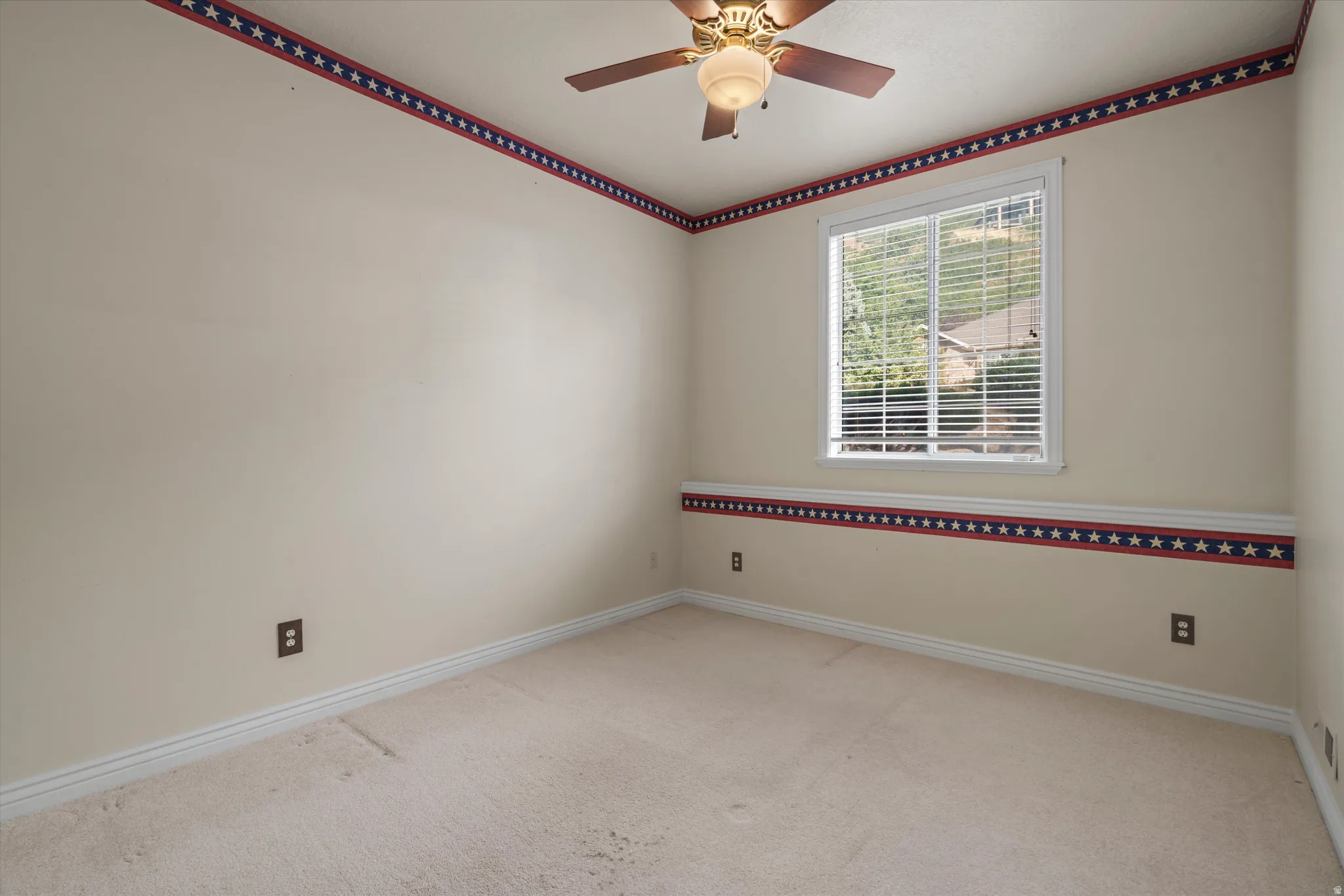Carpeted room with a ceiling fan light fixture and a window featuring white blinds