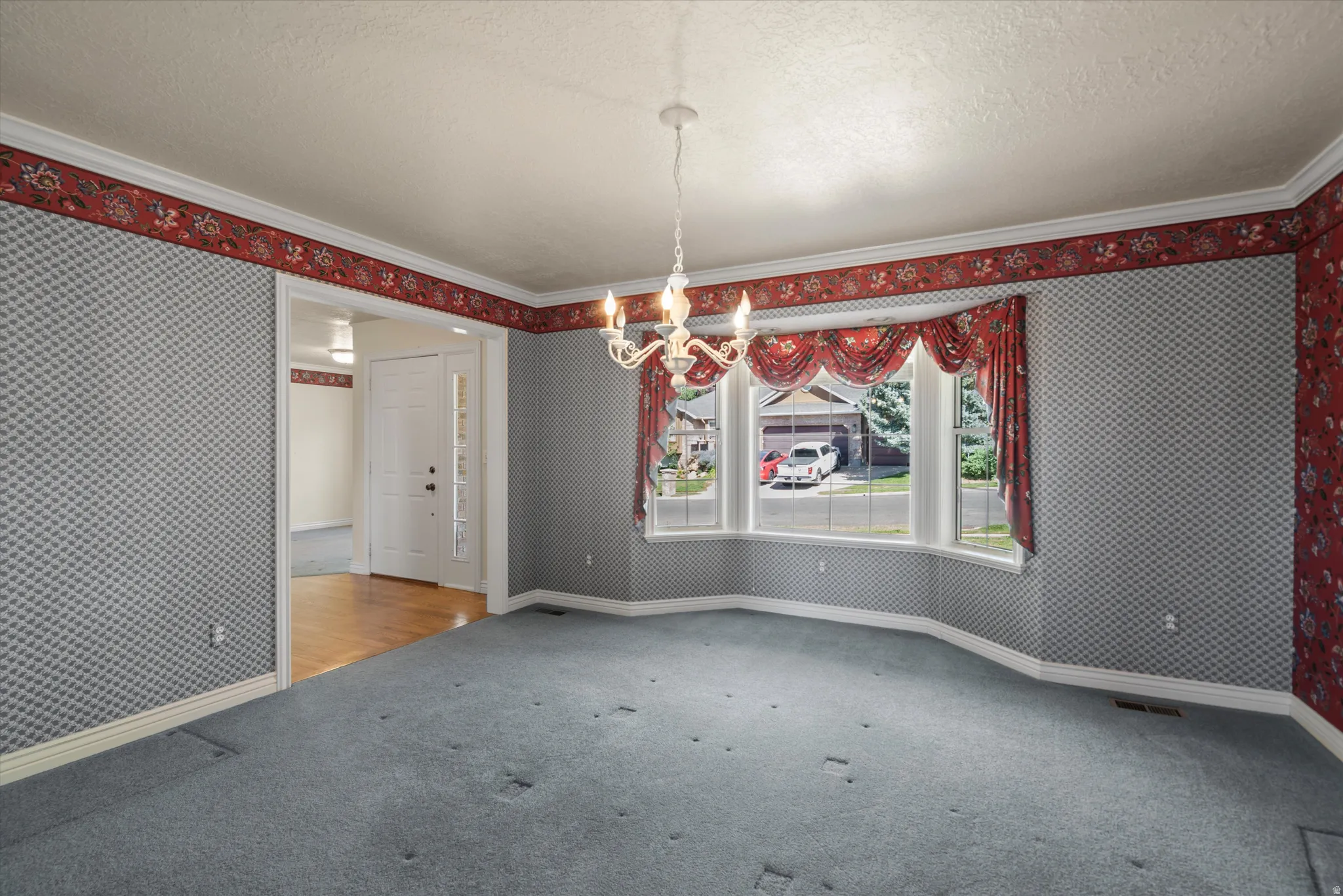 Spacious room featuring a bay window, crown molding, a decorative chandelier, and an open doorway to an entryway with wood-finish flooring