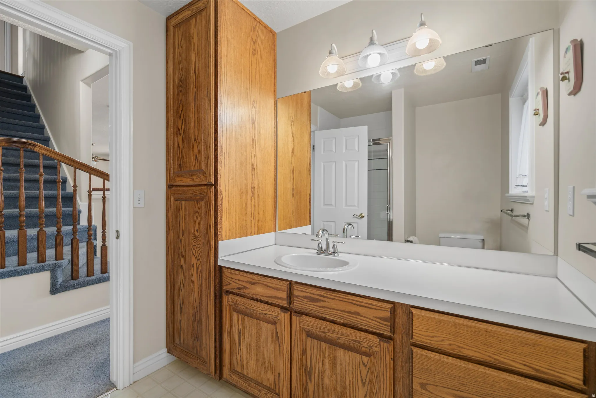 Bathroom vanity featuring wood-finish cabinetry, a single basin sink, and a large wall-mounted mirror