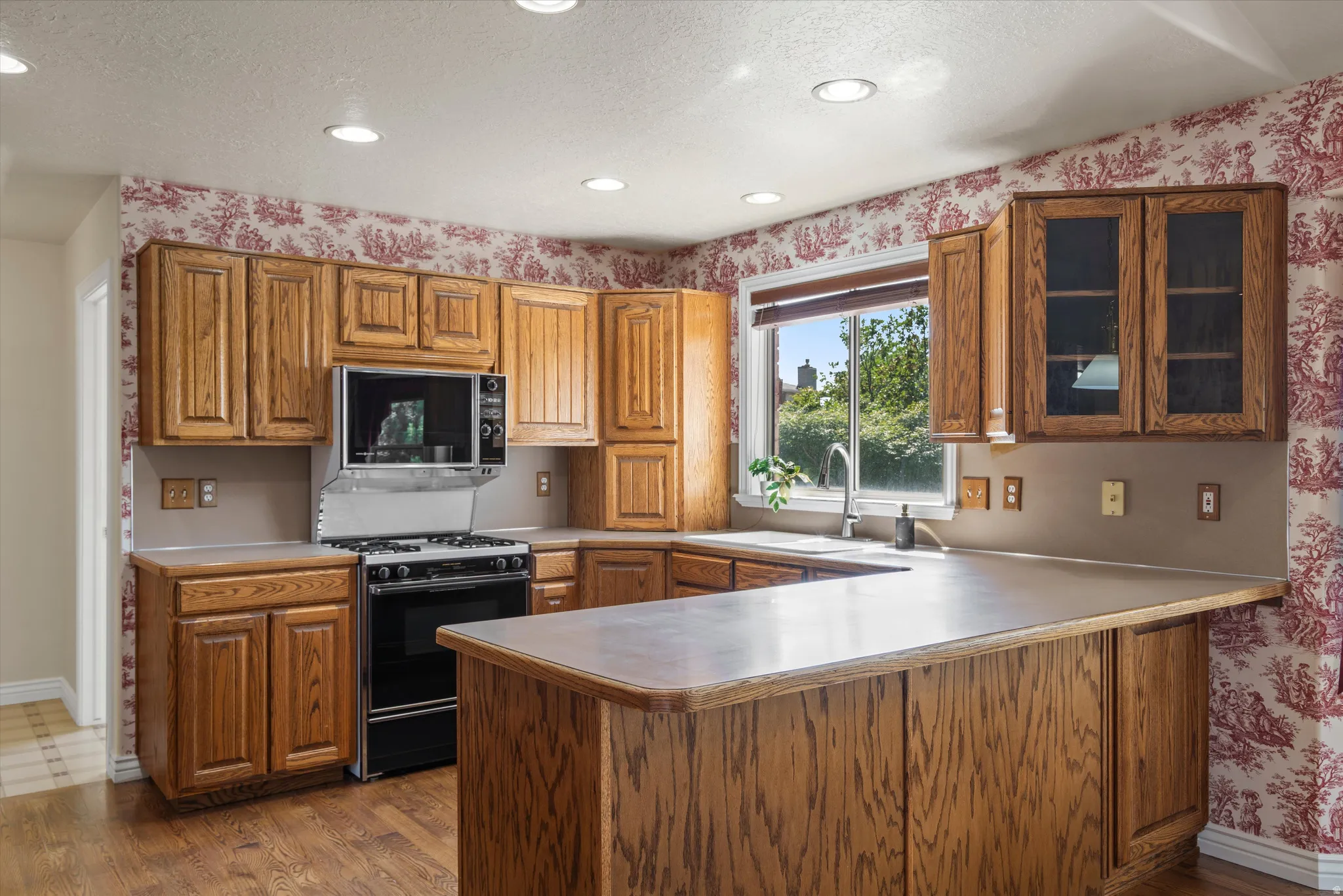 Kitchen featuring wood-finish cabinetry, a gas range, built-in microwave, and a double-basin sink under a window