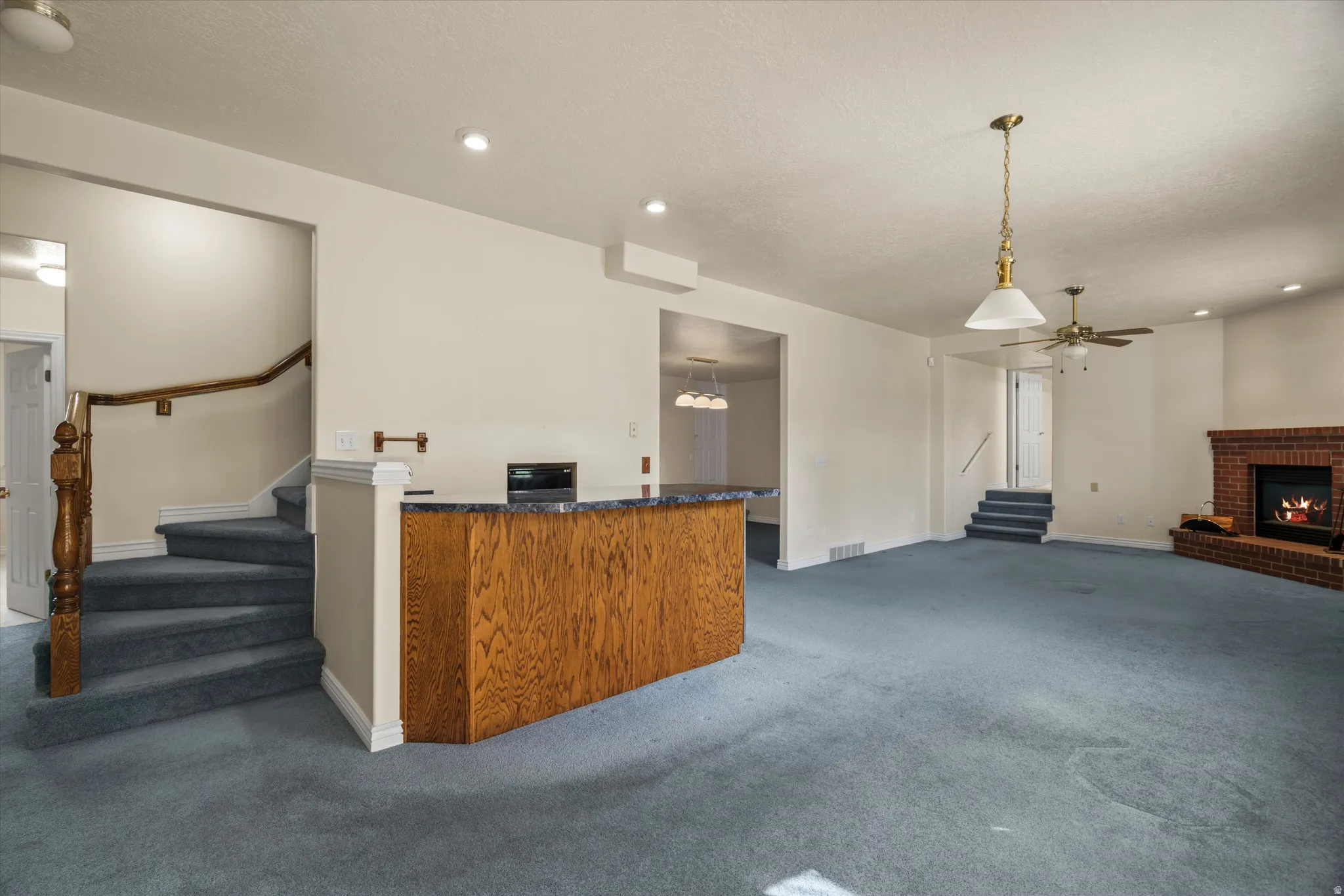 Spacious living area featuring a brick fireplace, built-in wet bar with a dark stone-look countertop, recessed lighting, and a ceiling fan