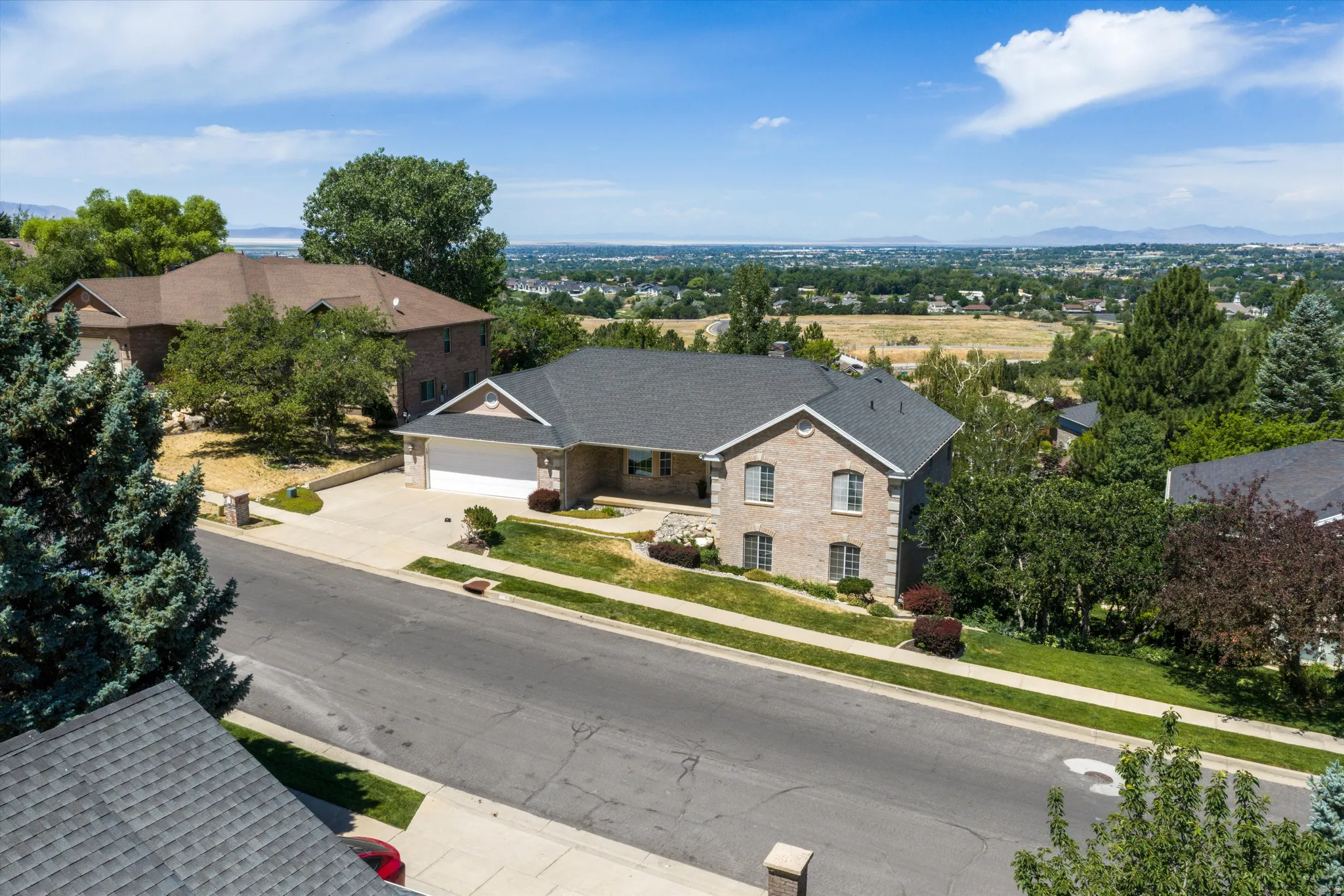Brick exterior residence featuring a dark shingle roof, integrated two-car garage, established front landscaping, and a paved driveway
