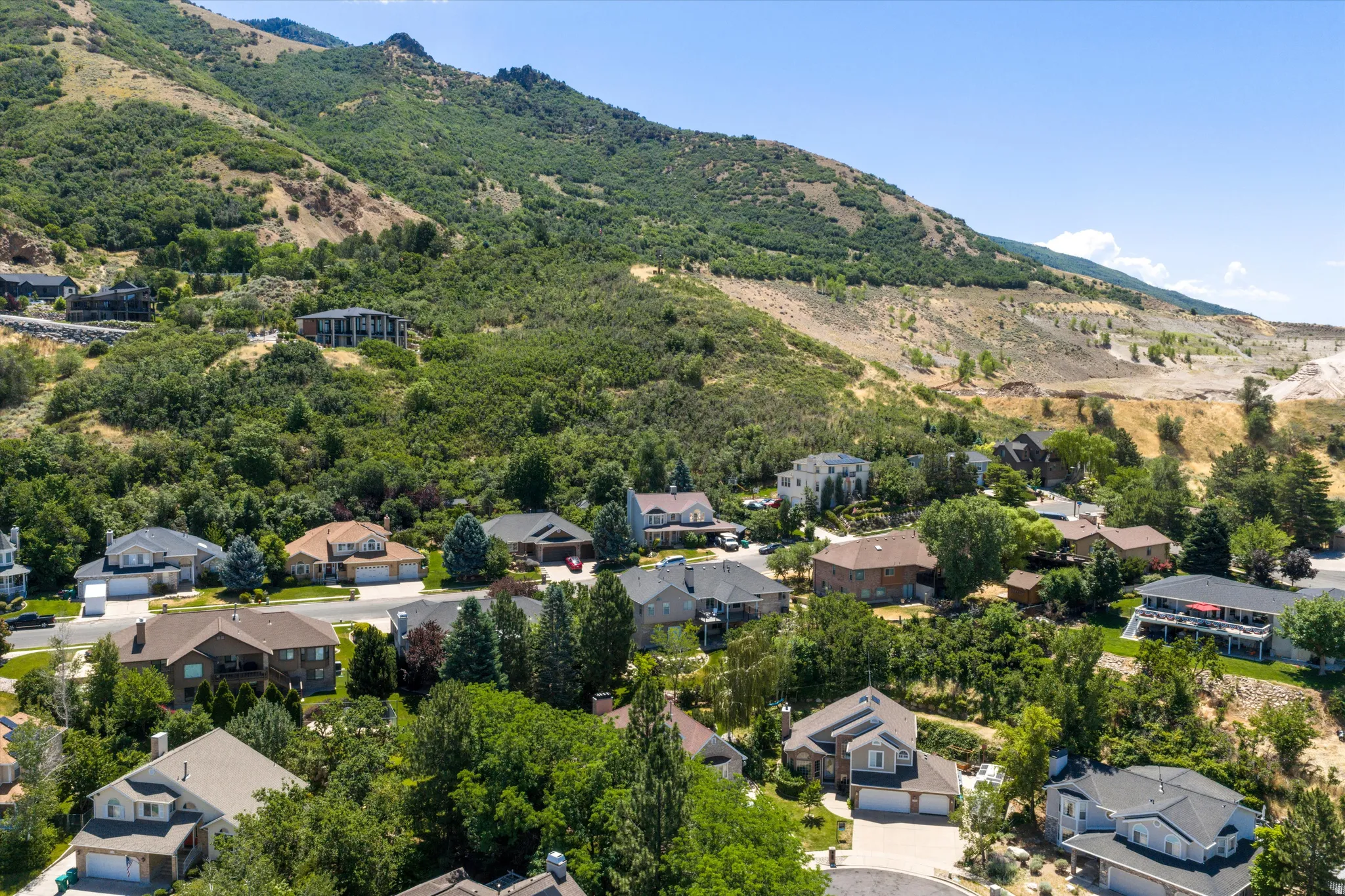 Residential community nestled against a verdant mountainside featuring a variety of architectural styles, mature landscaping, and paved streets