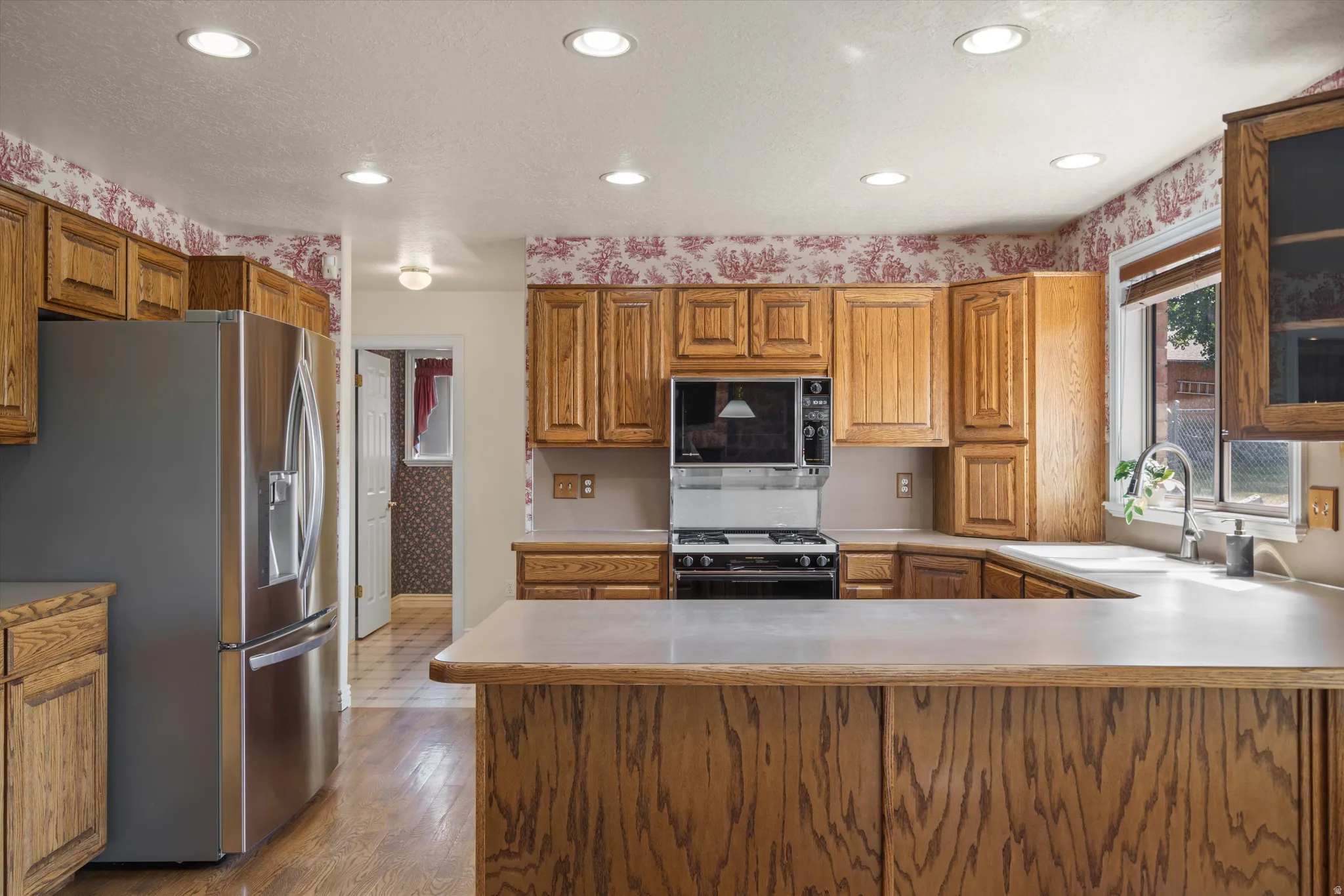 Kitchen featuring wood cabinetry, stainless steel appliances, recessed ceiling lights, and a window with natural light