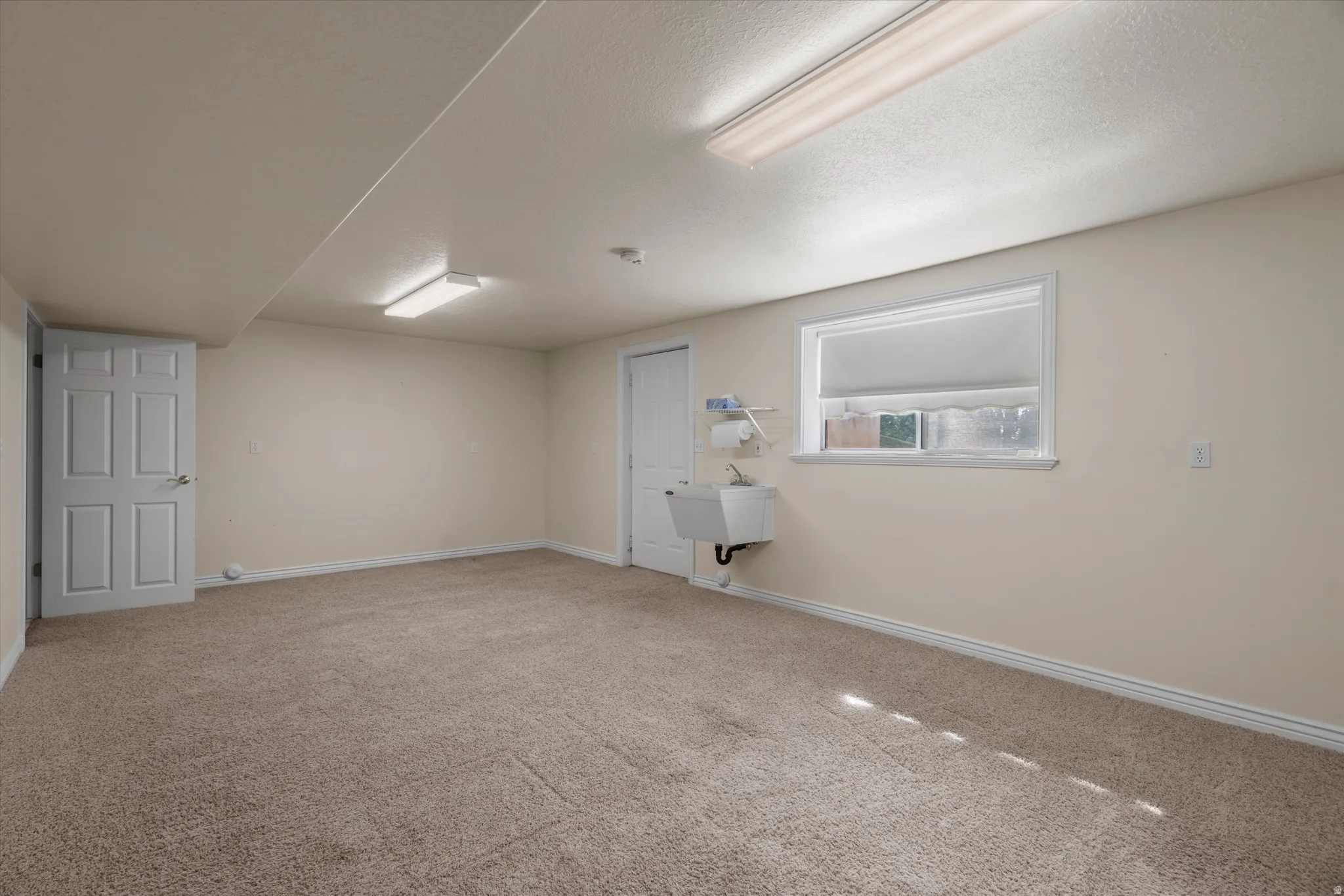 Carpeted room featuring a utility sink, a window with a white frame, and two interior doors
