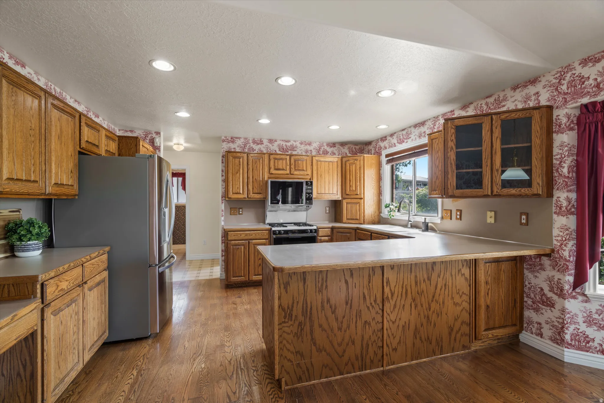 U-shaped kitchen featuring wood-finish cabinetry, a stainless steel refrigerator, and wood-finish flooring