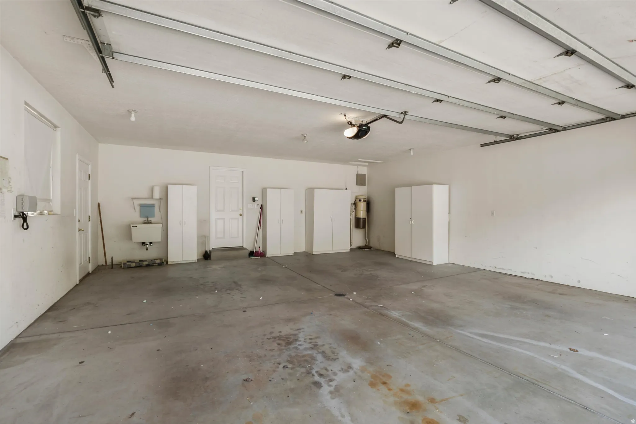 Spacious garage featuring a concrete floor, built-in cabinetry, utility sink, and overhead garage door opener