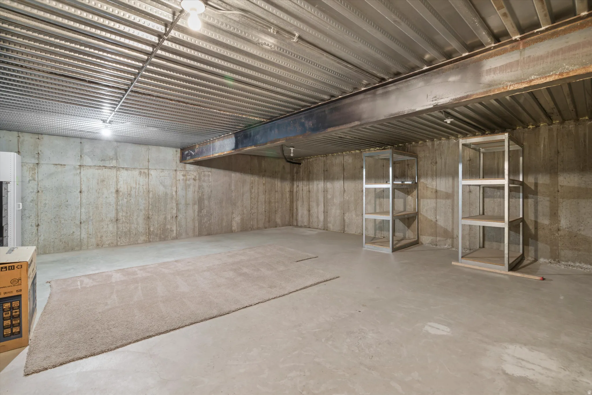Spacious unfinished basement offering concrete flooring, exposed corrugated metal ceiling, and a prominent structural beam