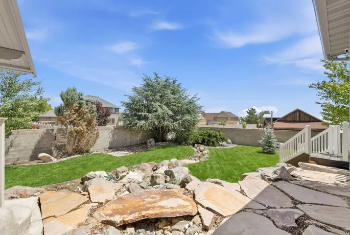 Landscaped backyard featuring a tiered design with a lush lawn, mature trees, a retaining wall, and a natural stone patio with flagstone stepping stones