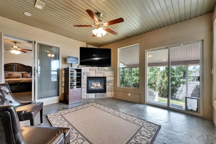 Covered patio featuring a corner stone fireplace, a ceiling fan with integrated lighting, and multiple sliding glass doors