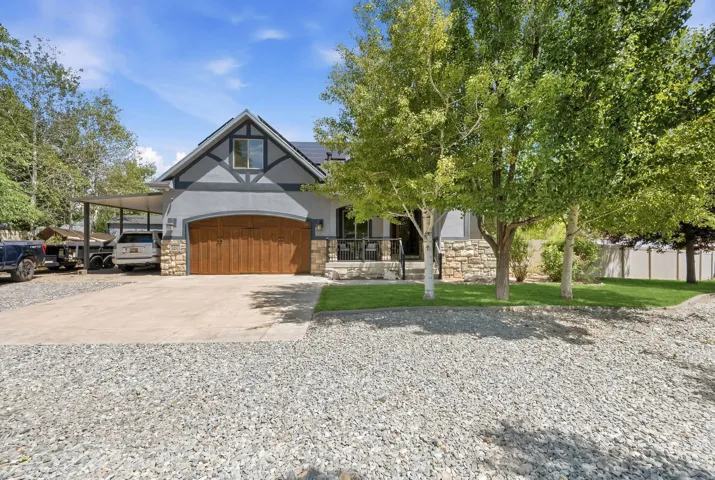 Exterior featuring gabled roofline, stone facade accents, wood-finish garage door, and a covered side parking area