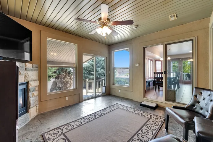 Sunroom featuring stamped concrete flooring, a stone-faced fireplace, a ceiling fan with integrated lighting, and multiple large windows