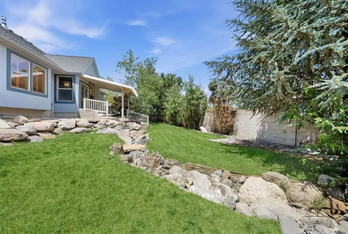Expansive backyard featuring a manicured lawn, established landscaping, and a multi-level rock garden feature